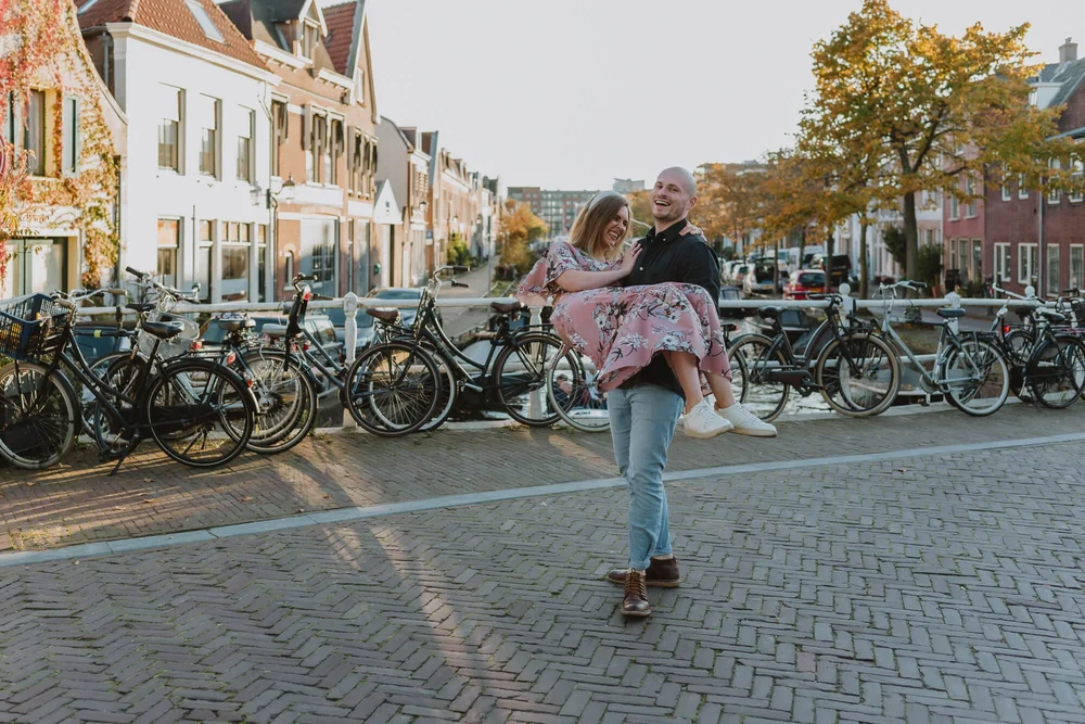 Engaged Couple in Haarlem centrum, he is lifting her in the air and swinging her around while standing on a bridge surrounded by bicycles.