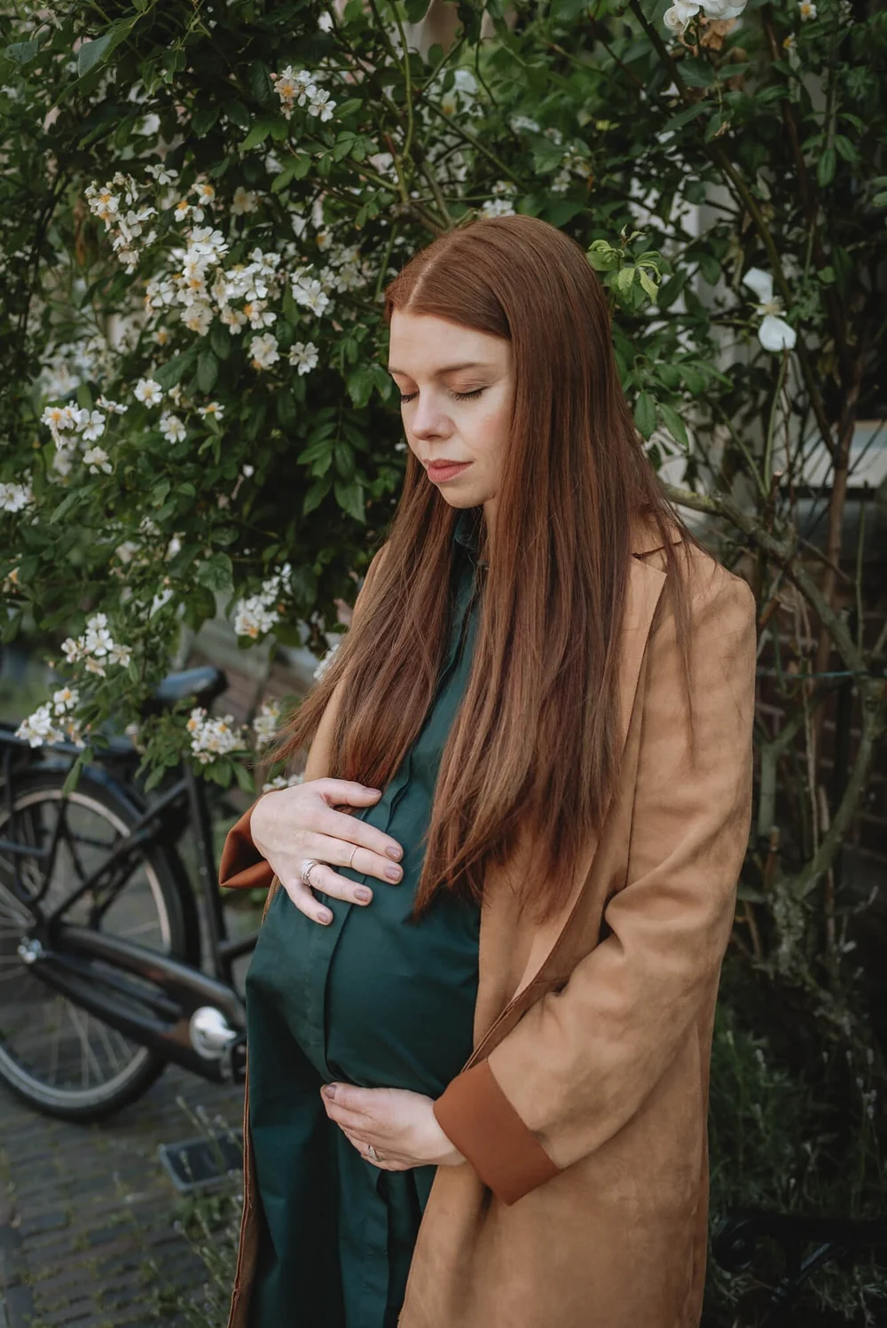Pregnant mommy holding her tummy standing in front of a floral plant in the street in Haarlem, the Netherlands