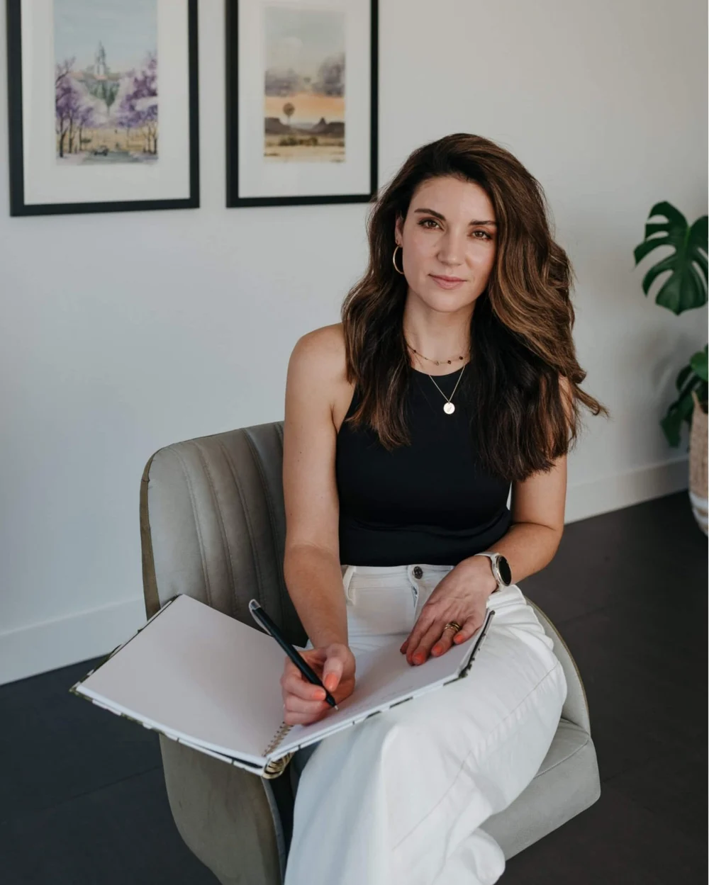 Business woman sitting in a chair wearing a black top and white pants