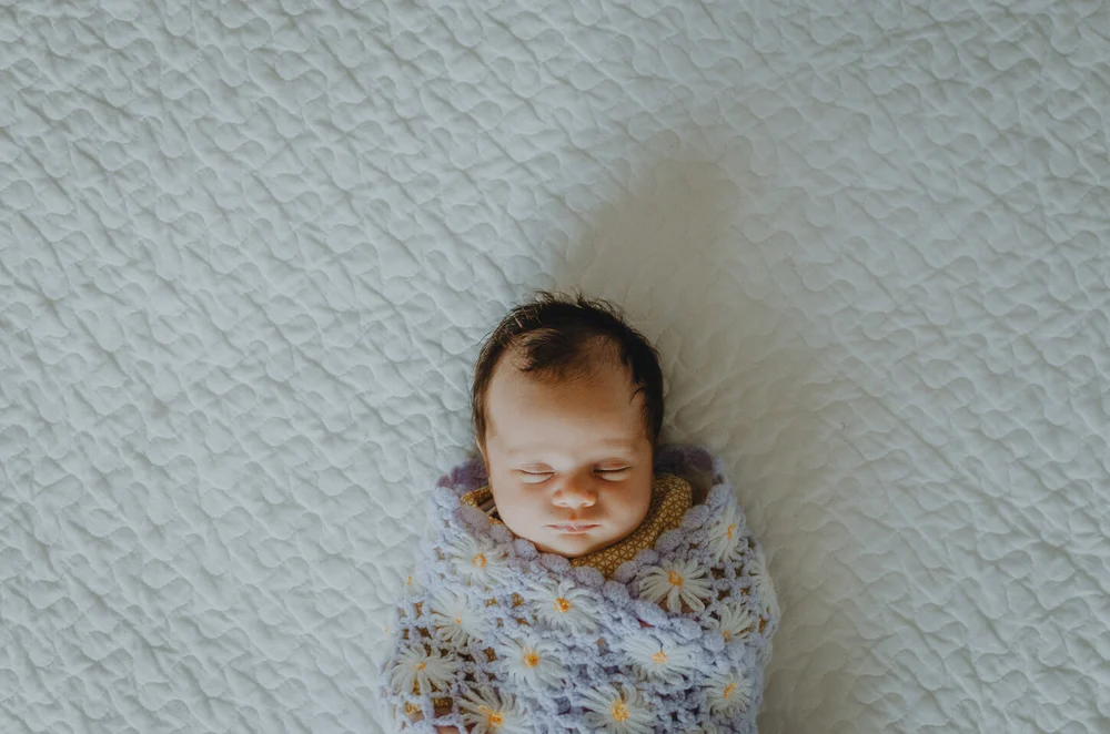 Newborn lying on a bed with wrapped in a floral blanket