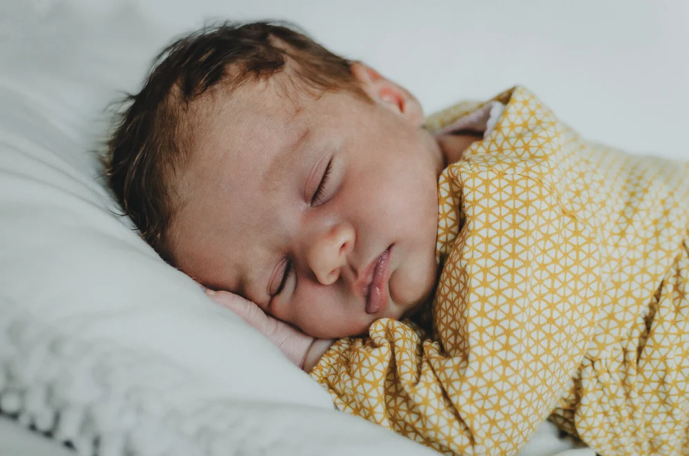Newborn baby in a yellow dress lying one her stomach while sleeping