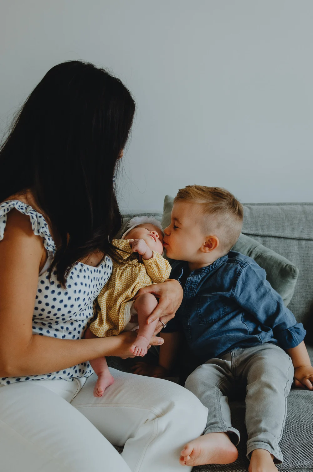 Brother kissing his newborn sister while mom is holding her
