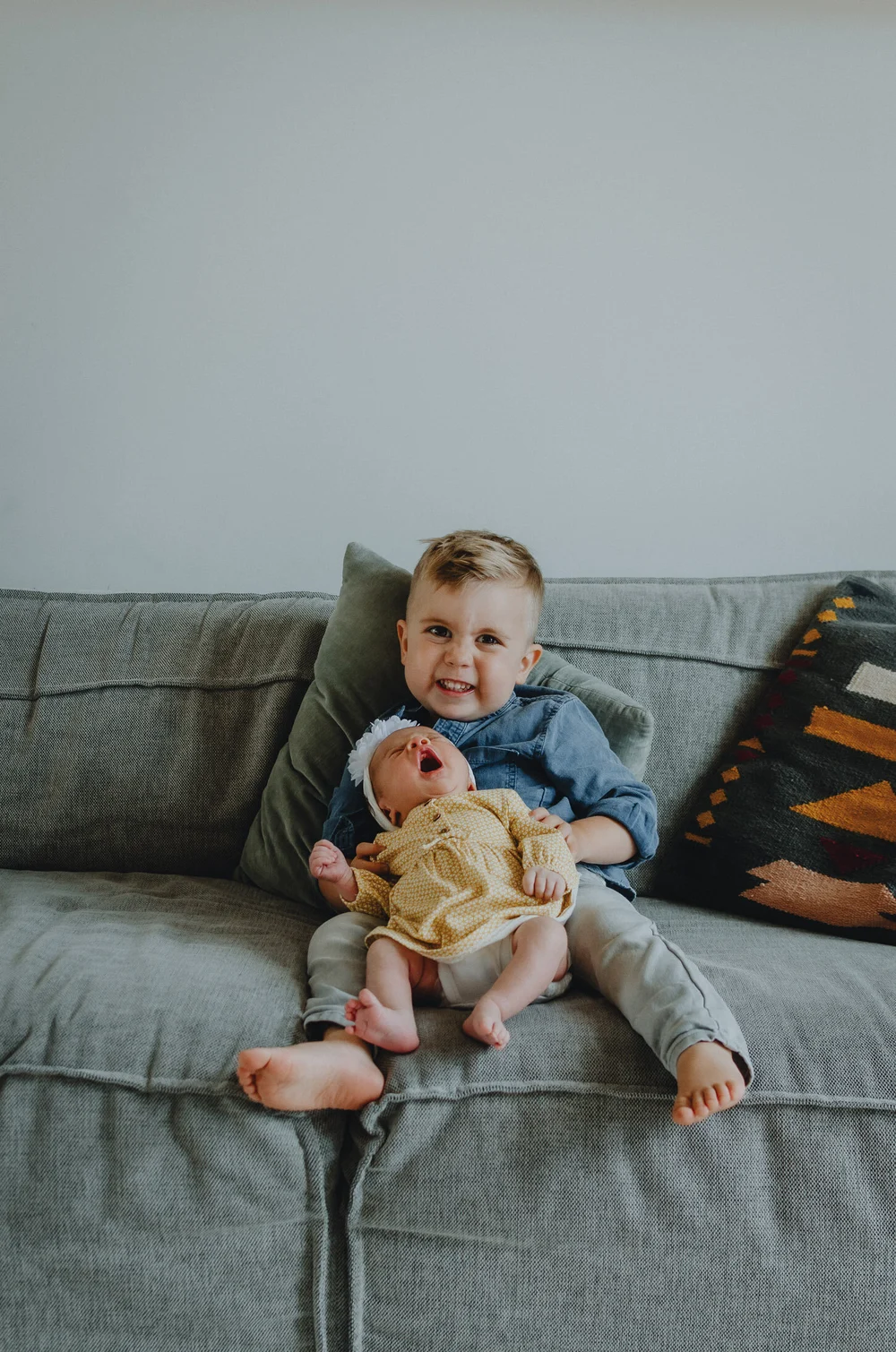 Newborn baby held by her big brother while they are sitting on a coach