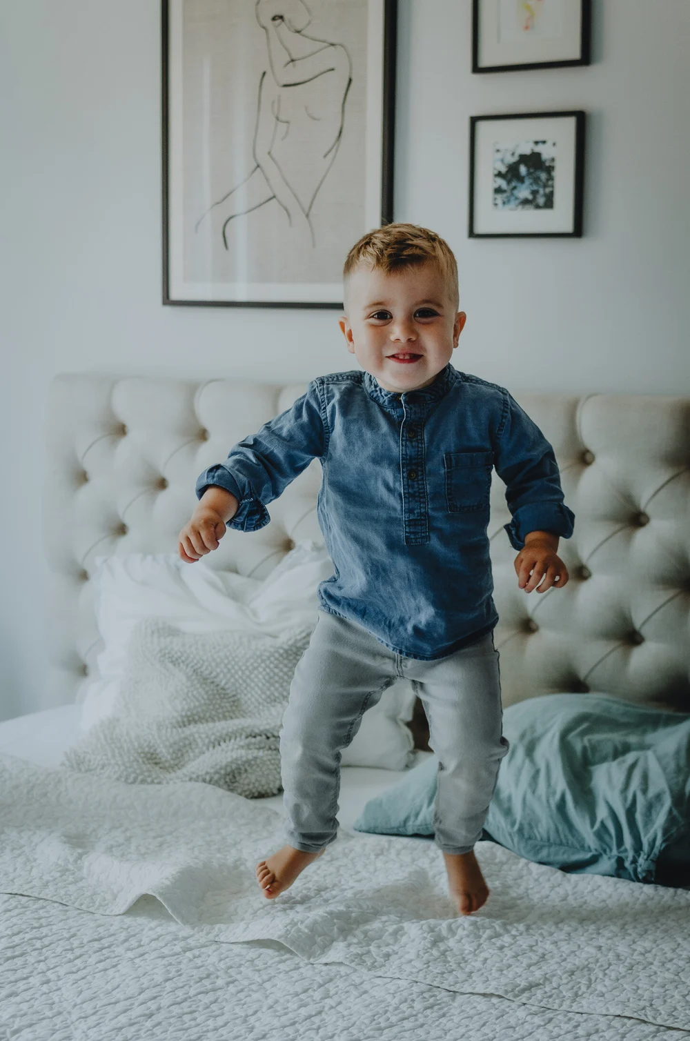 Big brother is jumping on the bed in a cute denim outfit.