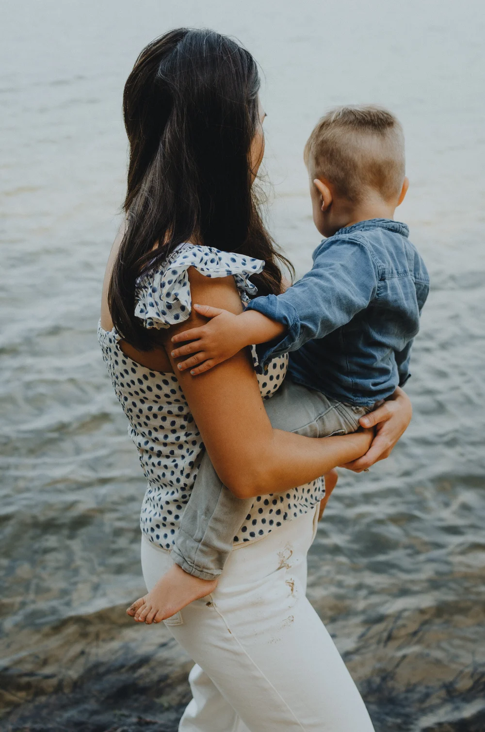 Mom holding her son next to a lake facing away from the camera
