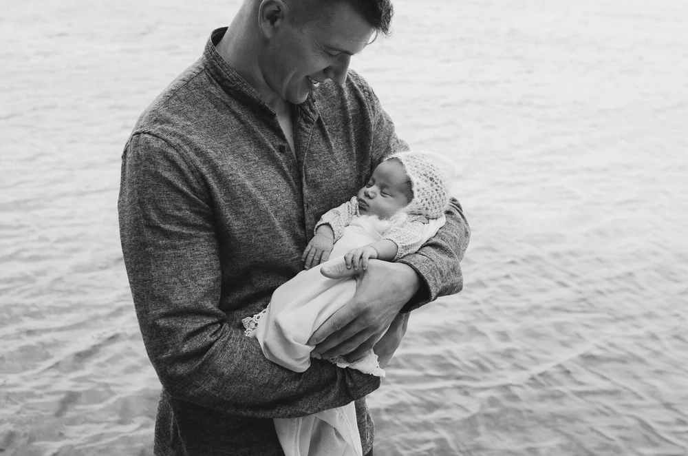 Dad holding his newborn baby while standing next to a lake