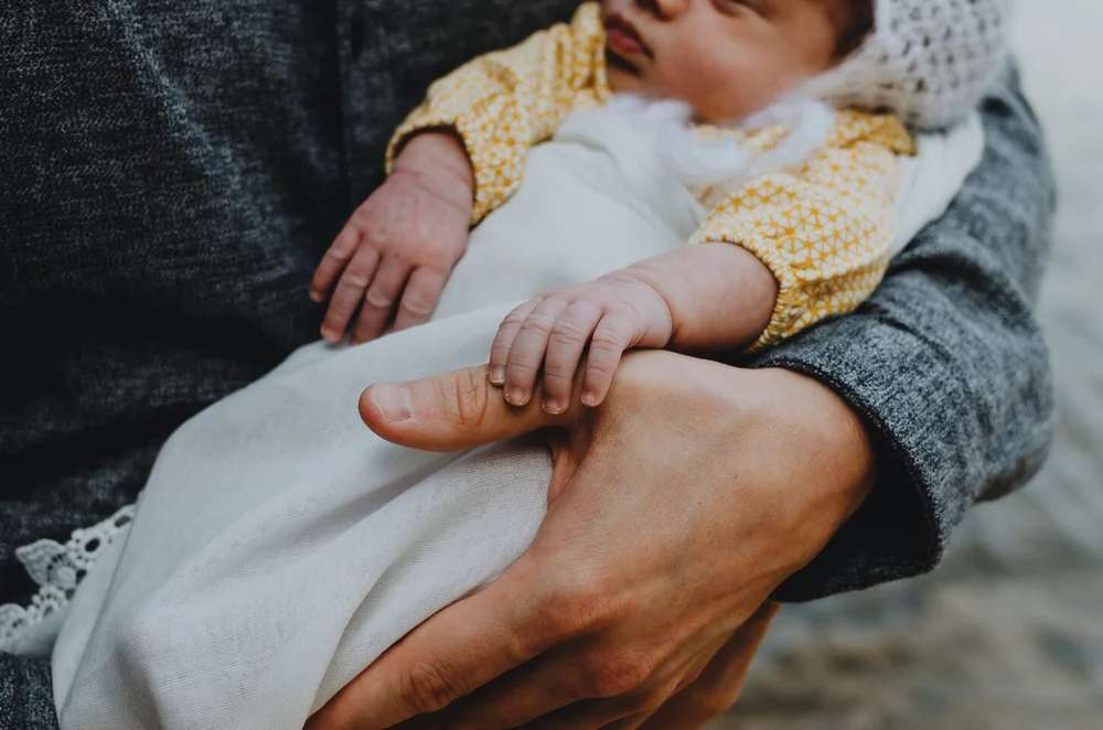 Little newborn fingers holding onto dad's thumb