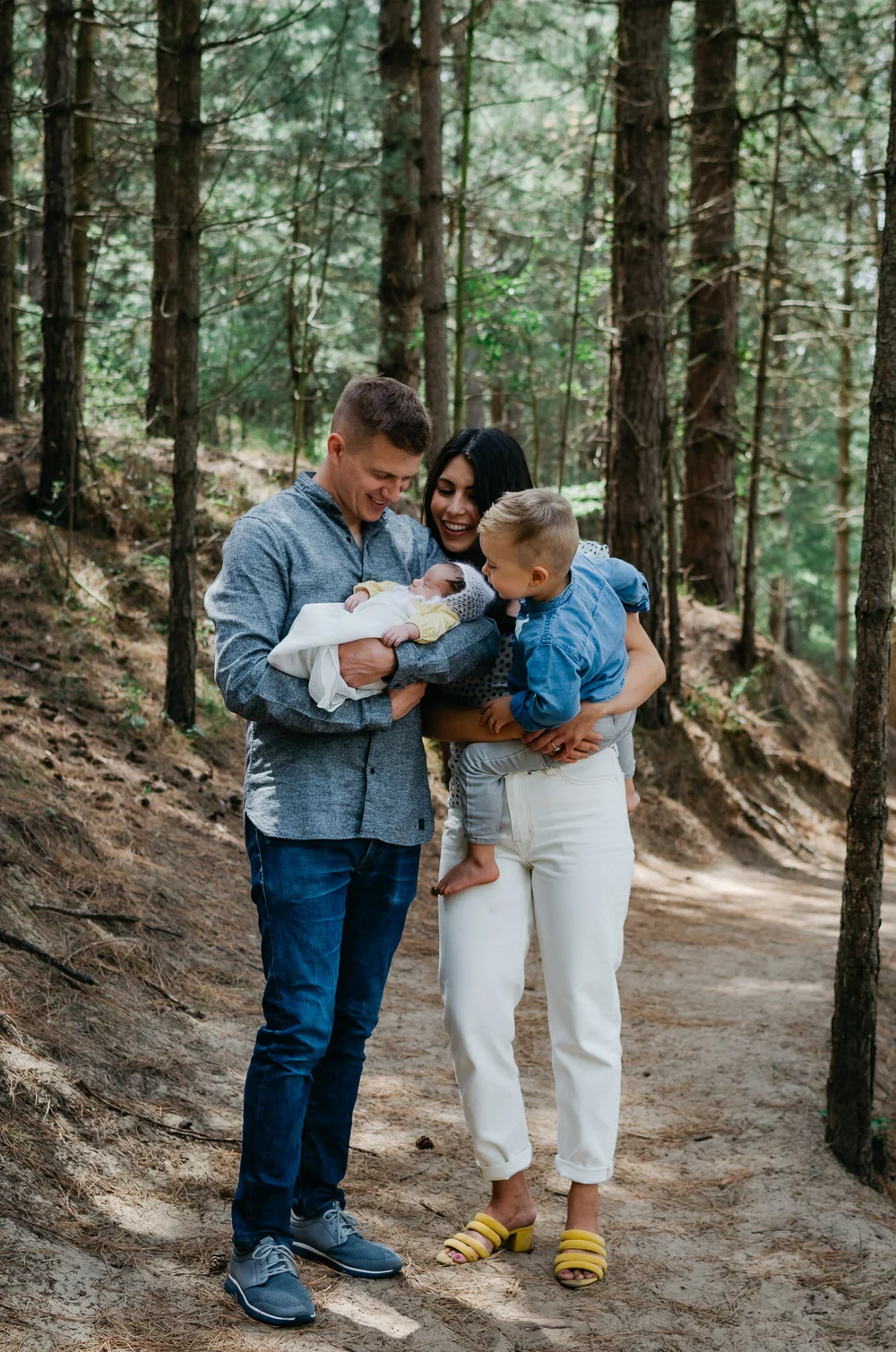 Family photo of mom, dad, son and newborn baby girl in a yellow dress standing in a forrest