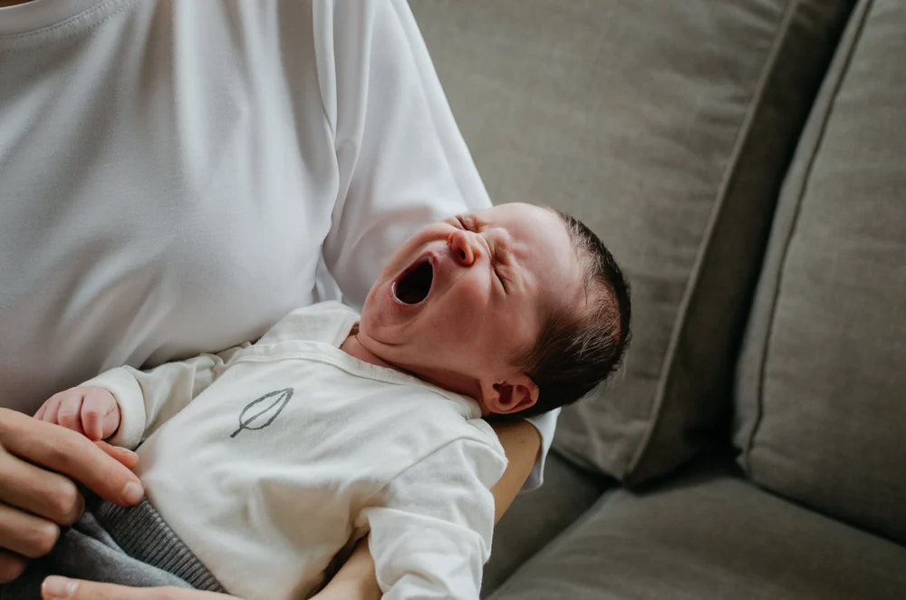 Newborn baby held by mom giving a big yawn