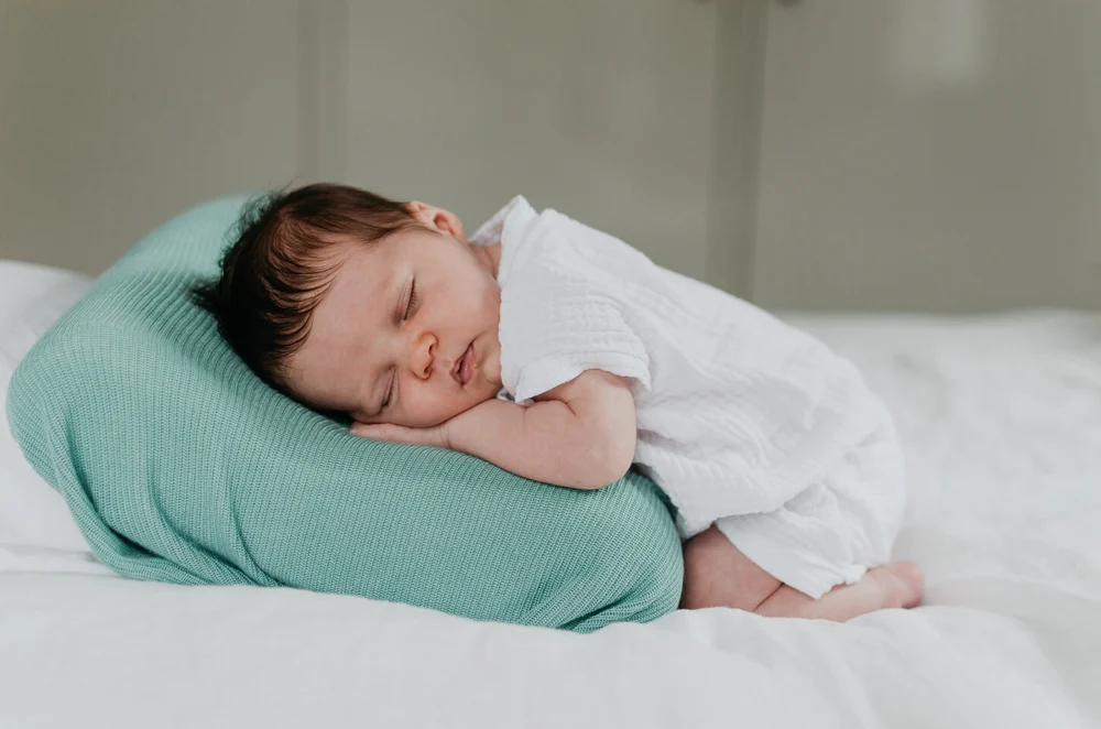 Newborn baby lying on her tummy on a bed posed in a relaxed position on a blue pillow