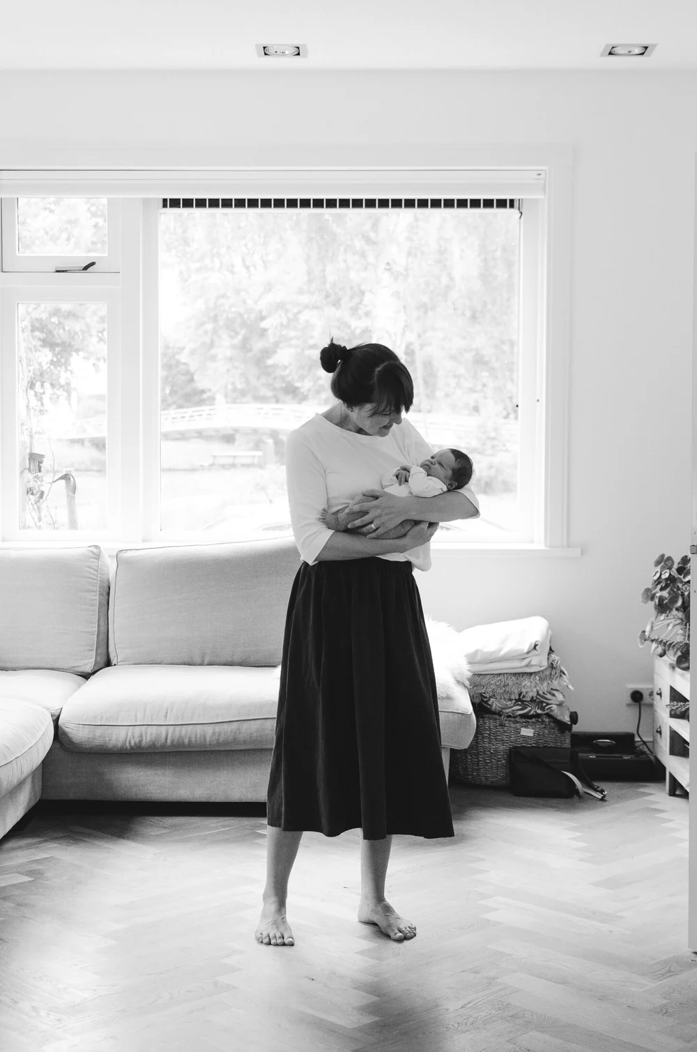 Mommy holding her newborn baby while she is standing in a wide open space in the living room