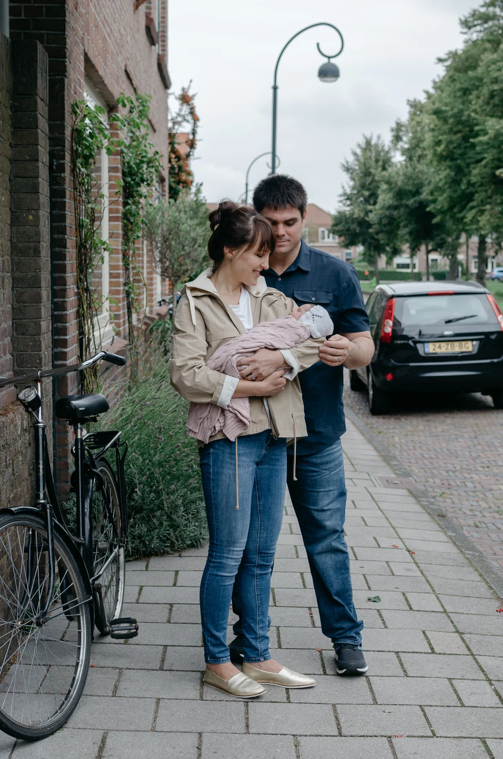 Family standing in front of their Dutch house holding their newborn baby