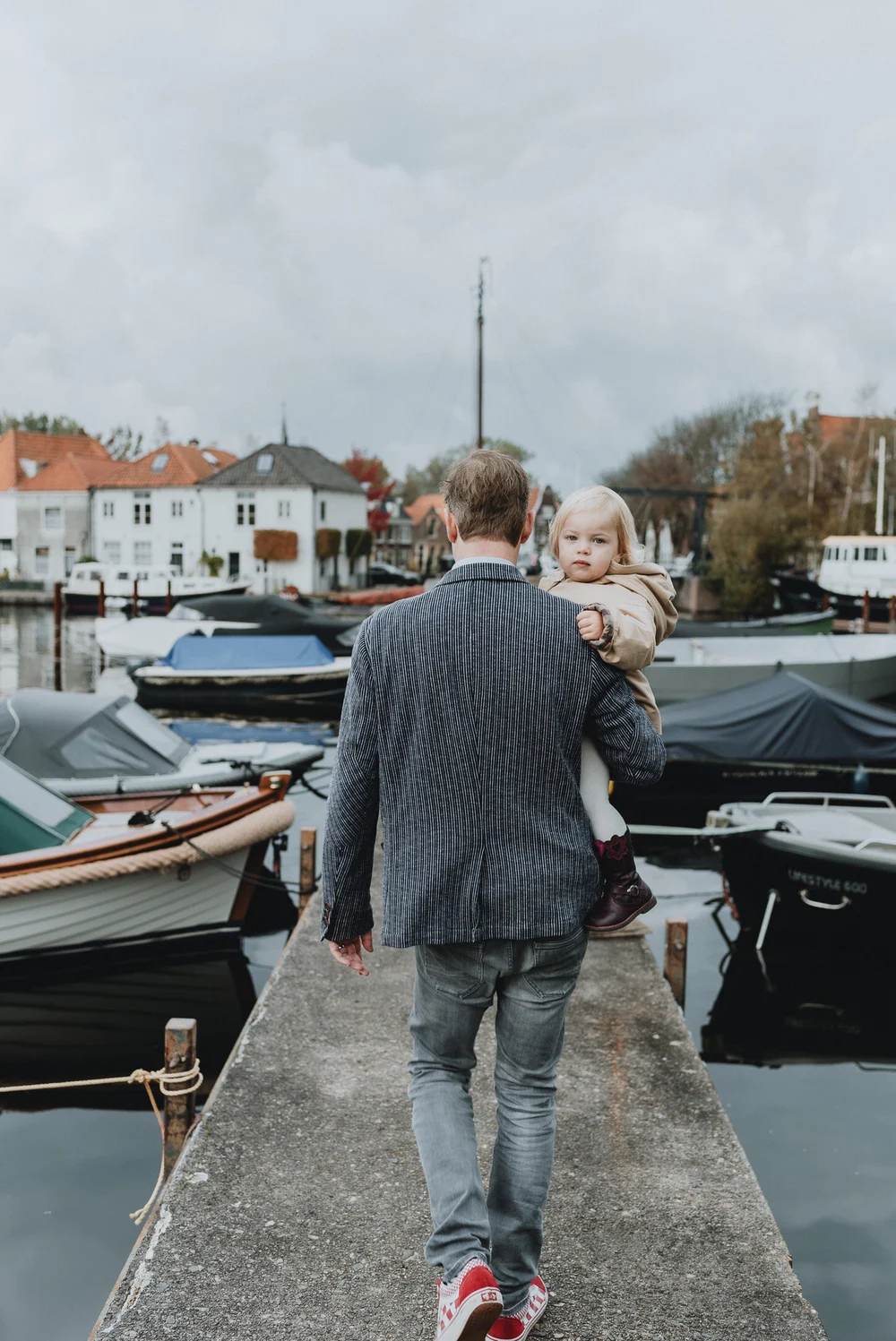 Dad walking with his daughter on bridge with boats and Dutch houses next to them and a dark, stormy clouds in the air.