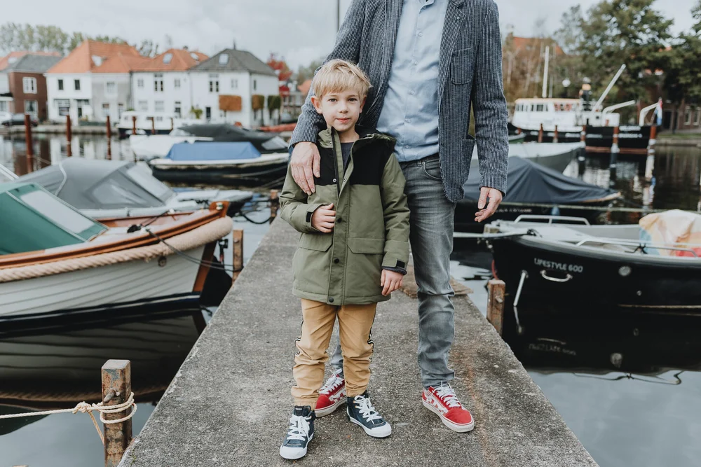 Dad holding onto his son, the are standing on a bridge next to boats and with Dutch houses in the background.