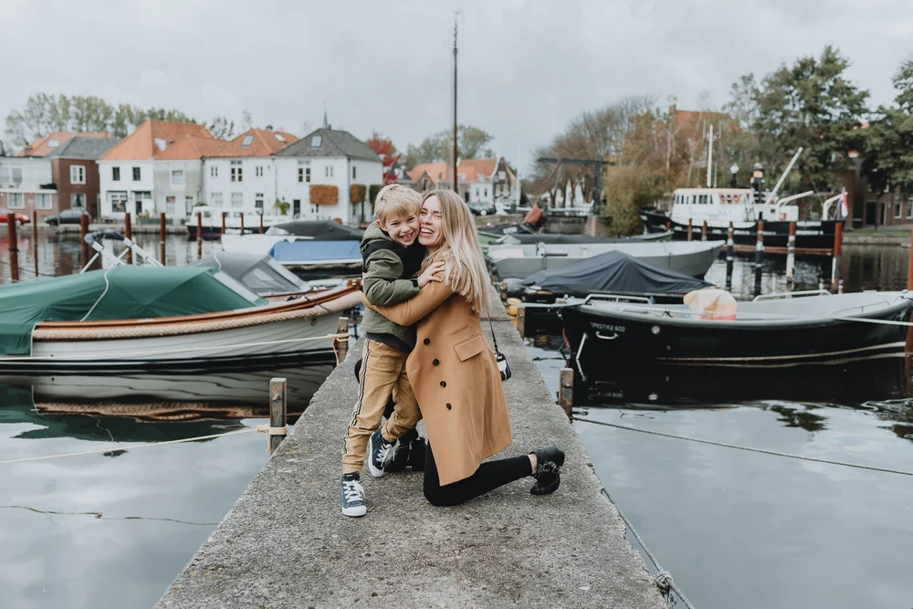 Mom and son holding each other with boats and Dutch houses in the background in Spaarndam