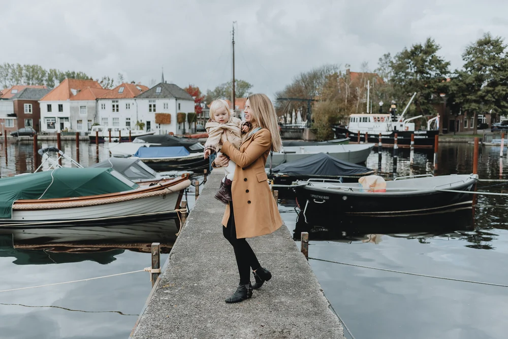 Mom swinging her daughter while walking over a small bridge with boats and Dutch houses around them, taken during a family photoshoot.