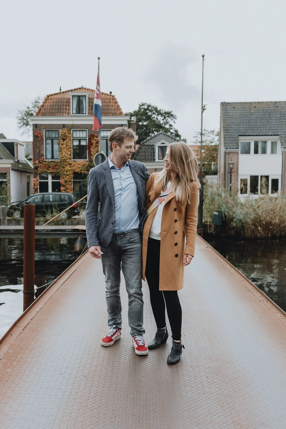 Couple standing on a bridge with a beautiful Dutch house in the background, photo was taken during a family photoshoot in Spraarndam.