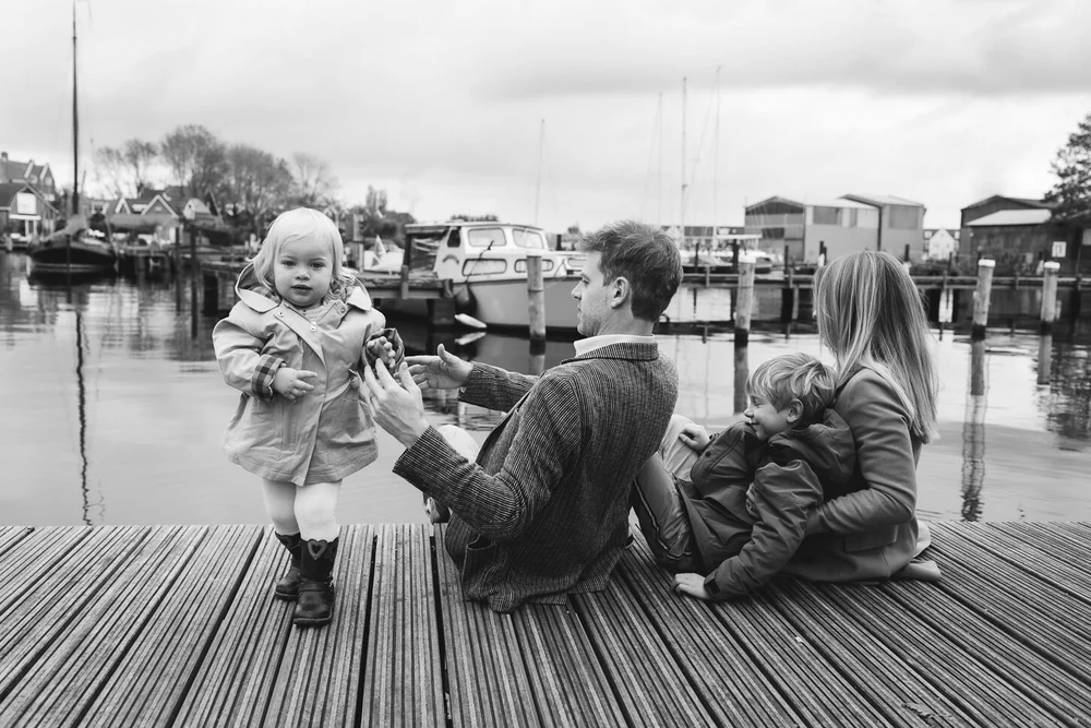 Family sitting on the dock next to boats, black and white image