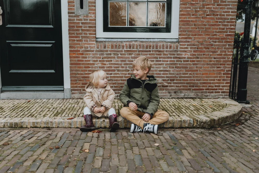 Brother and sister sitting next to each other on a bricked street corner, image taken during a family photoshoot in Spaarndam