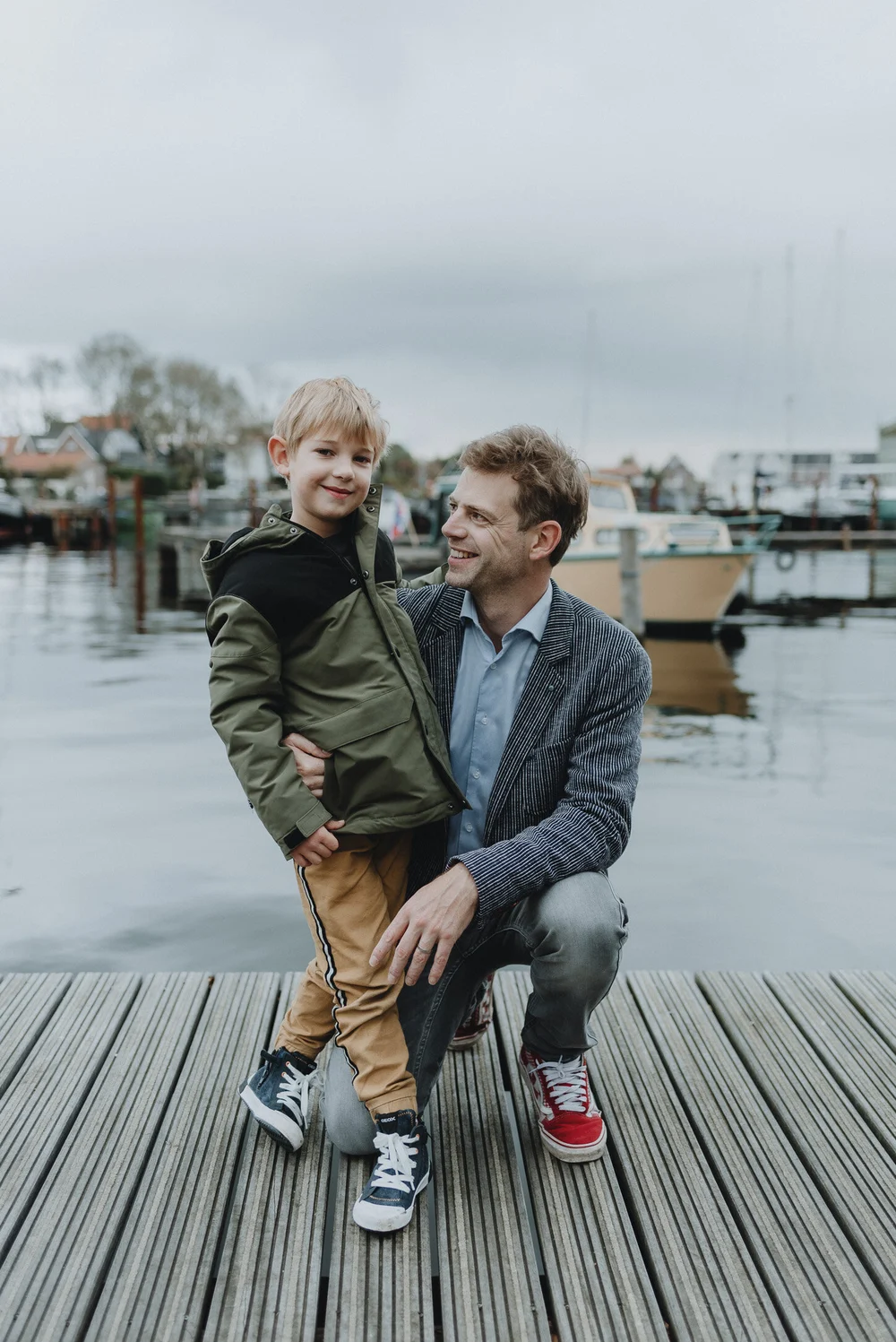 Father holding on to his son while standing on a dock with boats in the background in the Dutch village of Spaarndam.
