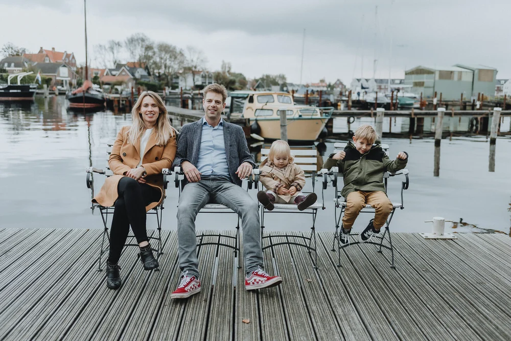 Family photo of four sitting in chairs on the dock with boats and Dutch houses in the background