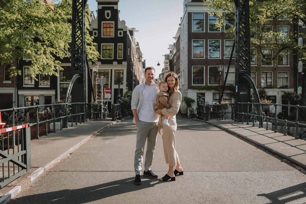Family photoshoot in Amsterdam on a bridge with Dutch houses in the background. Family standing together on Brouwersgracht