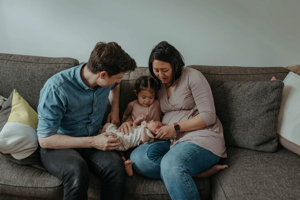 Family sitting on the couch while holding a newborn baby.