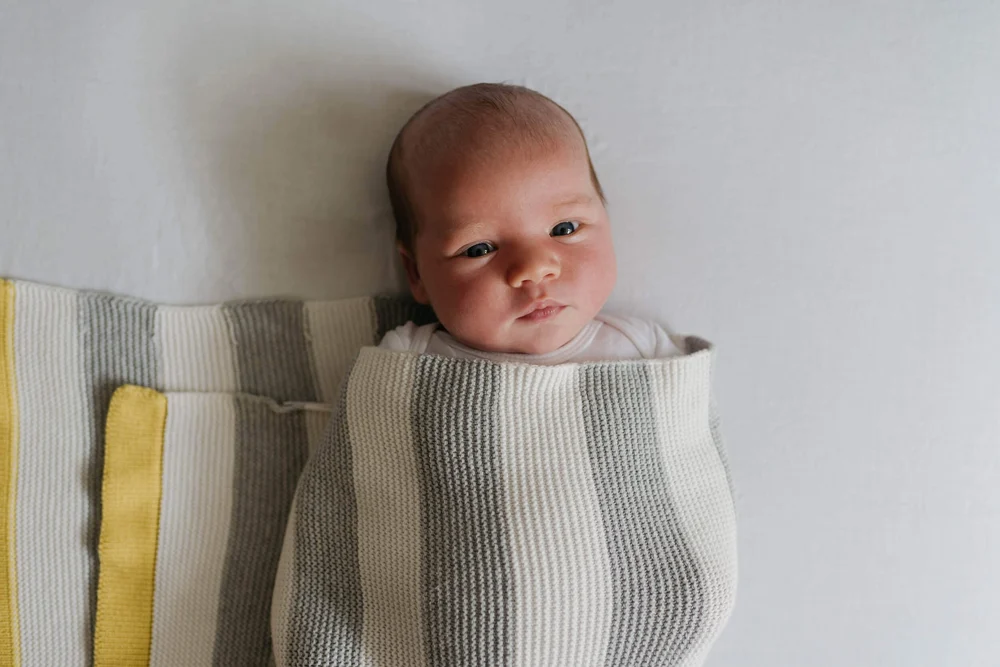 Newborn baby boy wrapped in a knitted blanket staring up at the camera