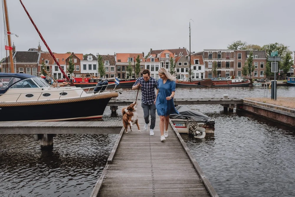 Couple running on the dock with their dog with boats and Dutch houses in the background
