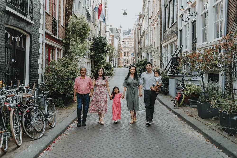 Family from America holding hands while walking down a beautiful street in Amsterdam while on holiday.