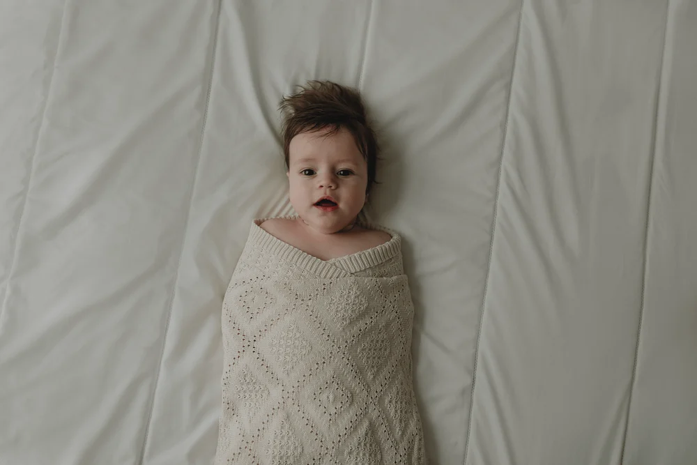Baby wrapped in a blanket lying on a bed during newborn photoshoot by Vicky McLachlan Photography